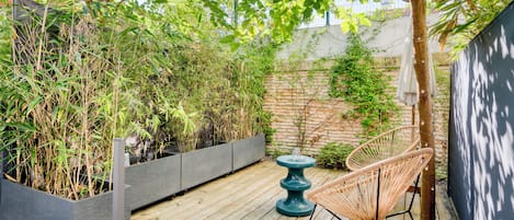A wooden deck with a planter box, a wicker chair, and a tree.