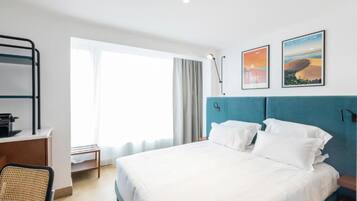 Ein Hotelzimmer mit Bett, Schreibtisch, Stuhl und großen Fenstern.