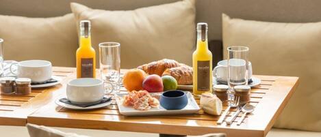 A breakfast setup with a croissant, fruits, and juice on a wooden table.