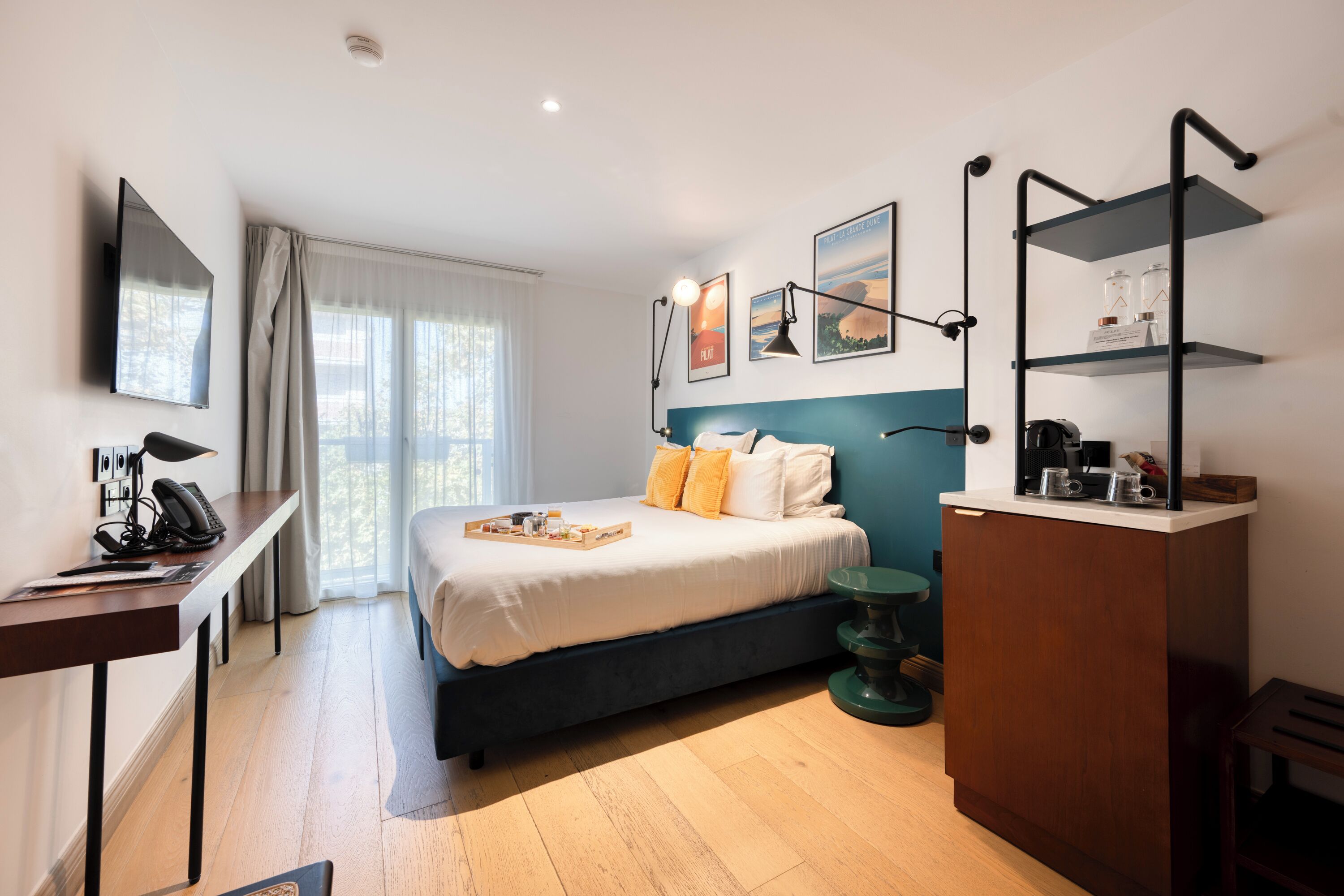 A modern hotel room with a bed, desk, and shelves.