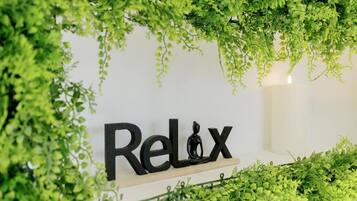 A wall with the word "Relax" and a meditating figure, surrounded by lush green foliage.