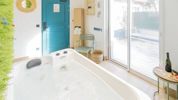 A bathroom with a bathtub, a blue door, a green chair, and a window with a view of the outside.