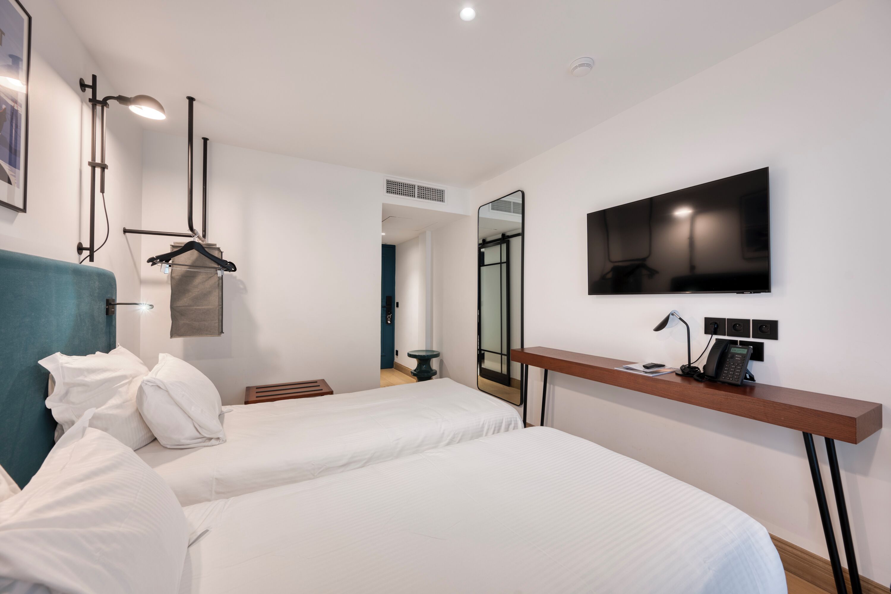 A hotel room with two beds, a TV, a desk with a phone, and a mirror.