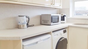 A compact kitchenette with a coffee maker, microwave, and washing machine. - Princess Court Apartment (Llanelli)