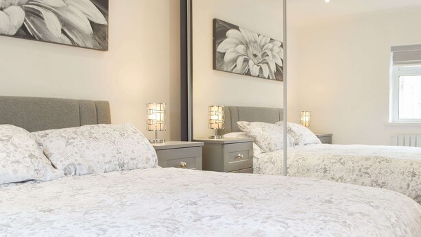 A bedroom with two beds, a large mirror, and wall-mounted lamps. - Princess Court Apartment (Llanelli)