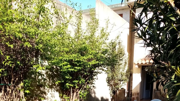A stone-paved courtyard with a table and chairs, surrounded by greenery and a building.