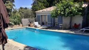 A clear blue swimming pool with lounge chairs and a small building with shutters. - mas (La Londe les Maures)