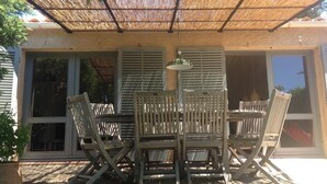 A covered patio with a table and chairs, large windows, and a hanging light fixture. - mas (La Londe les Maures)