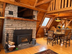 Un intérieur de chalet chaleureux avec une cheminée en pierre, un coin repas en bois et un plafond en pente.