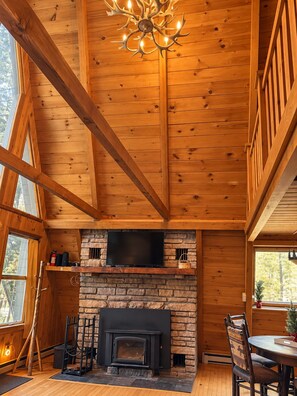 Un intérieur en bois avec une cheminée, un téléviseur fixé au-dessus et un lustre.
