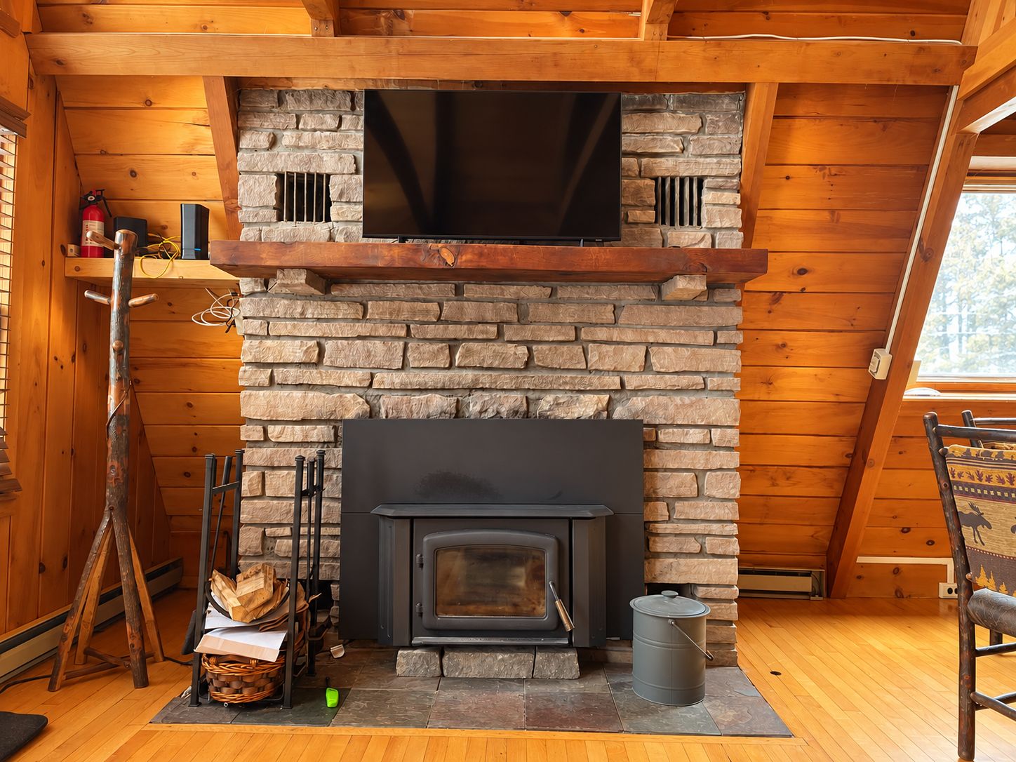 L’intérieur d’un chalet chaleureux, avec une cheminée en pierre, des murs en bois et une fenêtre.