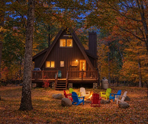 A cabin with a deck, surrounded by autumn leaves.