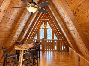 A wooden interior with a dining table and chairs, a ceiling fan, and a chandelier.