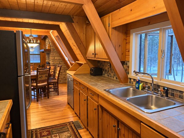 Une cuisine avec des meubles en bois, un évier à deux bacs et un coin repas comprenant une table et des chaises.