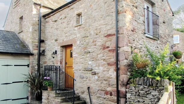 A stone building with a wooden door, a small window, and a metal railing. - The Hayloft - UK37563 (Crosby Garrett, near Kirkby Stephen)