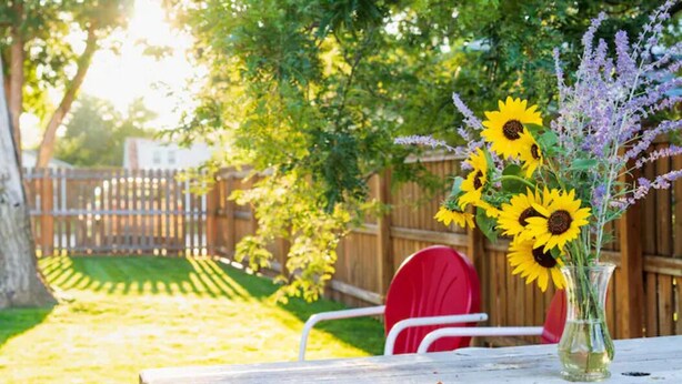 A wooden table with a vase of sunflowers and lavender, a red chair, and a wooden fence in the background.