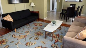 A living room with a black sofa, a beige sofa, a coffee table, and a TV.
