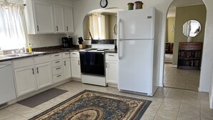 A kitchen with white cabinets, a stove, a refrigerator, and a patterned rug.