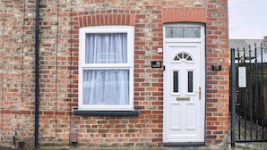 Una casa de ladrillo con una puerta blanca y dos ventanas, cada una con cortinas blancas.