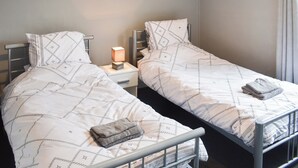 Habitación doble con dos camas, cada una con ropa de cama y almohadas estampadas, mesita de noche con lámpara y un cuadro en la pared.