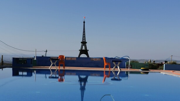 Una piscina con vistas a la Torre Eiffel, rodeada de sillas color naranja y un cartel que dice "Femme".