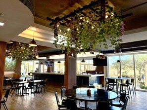 Un restaurant doté d’une salle à manger intérieure, de plantes suspendues et offrant une vue sur l’extérieur.