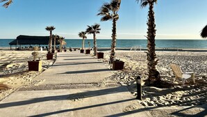 Ein Strandweg, gesäumt von Palmen, mit einem strohgedeckten Gebäude im Hintergrund.