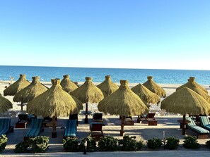 Een strandlounge met rieten parasols en gestreepte ligstoelen.