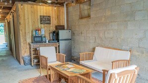 Une cuisine rustique avec des murs en bois, un réfrigérateur, un four à micro-ondes et une machine à café. On y trouve une table en bois avec des chaises et un tapis sur le sol.