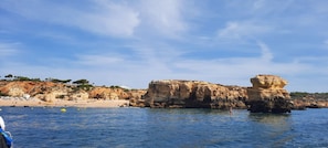 A coastal landscape with rocky cliffs, a beach, and clear blue water.