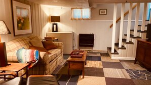 A cozy living room with a sofa, a coffee table, and a fireplace. There is a staircase in the background. - Cozy English Basement Apt quiet but close to downtown (Winchester)