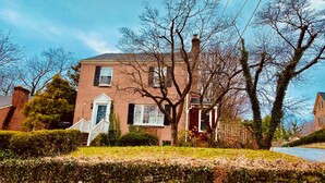 A two-story brick house with a front porch, a stone wall in the foreground, and leafless trees. - Cozy English Basement Apt quiet but close to downtown (Winchester)