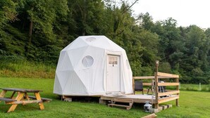 A geodesic dome tent with a door and windows, a wooden deck, and a picnic table.