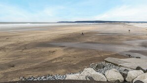 Una playa extensa con un primer plano rocoso y colinas al fondo.