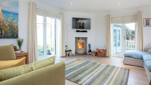 Amplia sala de estar con chimenea, un sofá, un televisor sobre la chimenea y ventanas grandes con cortinas.