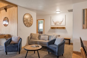 Un salon chaleureux avec un canapé, deux fauteuils, une table basse et un buffet en bois.