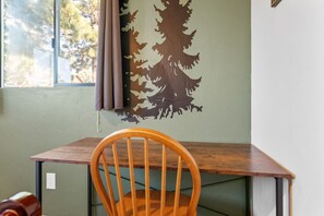 Een kamer met een houten tafel en een stoel, een raam met gordijnen, en een muur met een muurschildering van een boom.