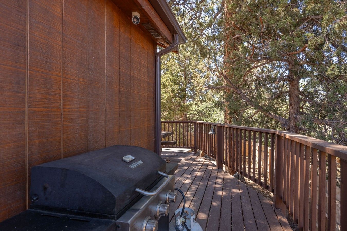 A wooden deck with a barbecue grill, surrounded by trees.