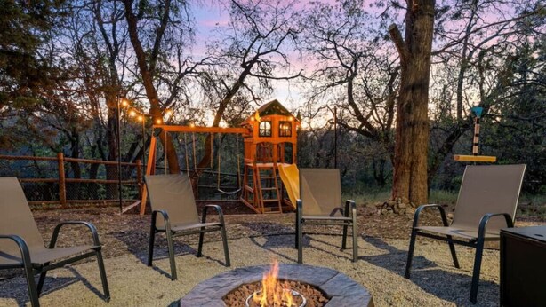 Un espacio al aire libre con una chimenea, sillas y un parque infantil.