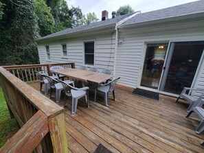 En terrasse med et træbord og stole, en skydedør samt udsigt til et hus med skorsten.