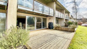 Un bâtiment à deux étages doté de grandes fenêtres en verre, d’une terrasse en bois et d’un espace jardin.