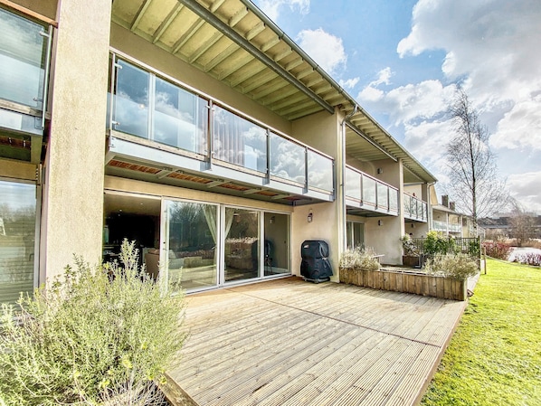 A two-story building with large glass windows, a wooden deck, and a garden area.