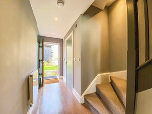 A hallway with a wooden floor leading to a staircase with carpeted steps.