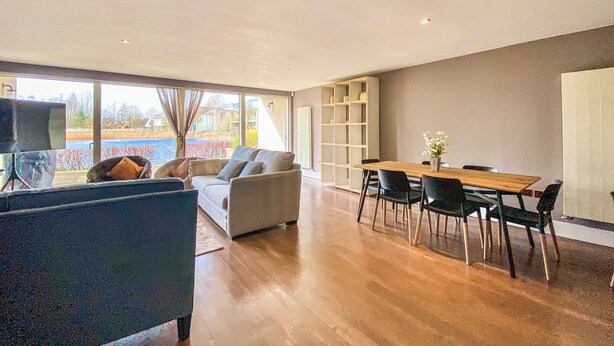 A spacious living area with a sofa, chairs, a dining table, and a bookshelf.