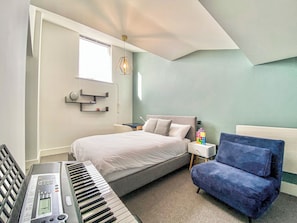 A bedroom with a bed, a desk with a keyboard, a chair, and a wall-mounted shelf with a clock.