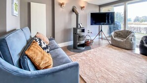 A modern living room with a blue sofa, a TV on a tripod, a fireplace, and a large window.