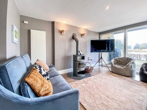 Una sala de estar moderna con un sofá azul, un televisor sobre un trípode, una chimenea y un ventanal grande.
