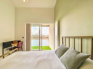 A hotel room with a bed, a desk, and a view of a body of water through a sliding door.