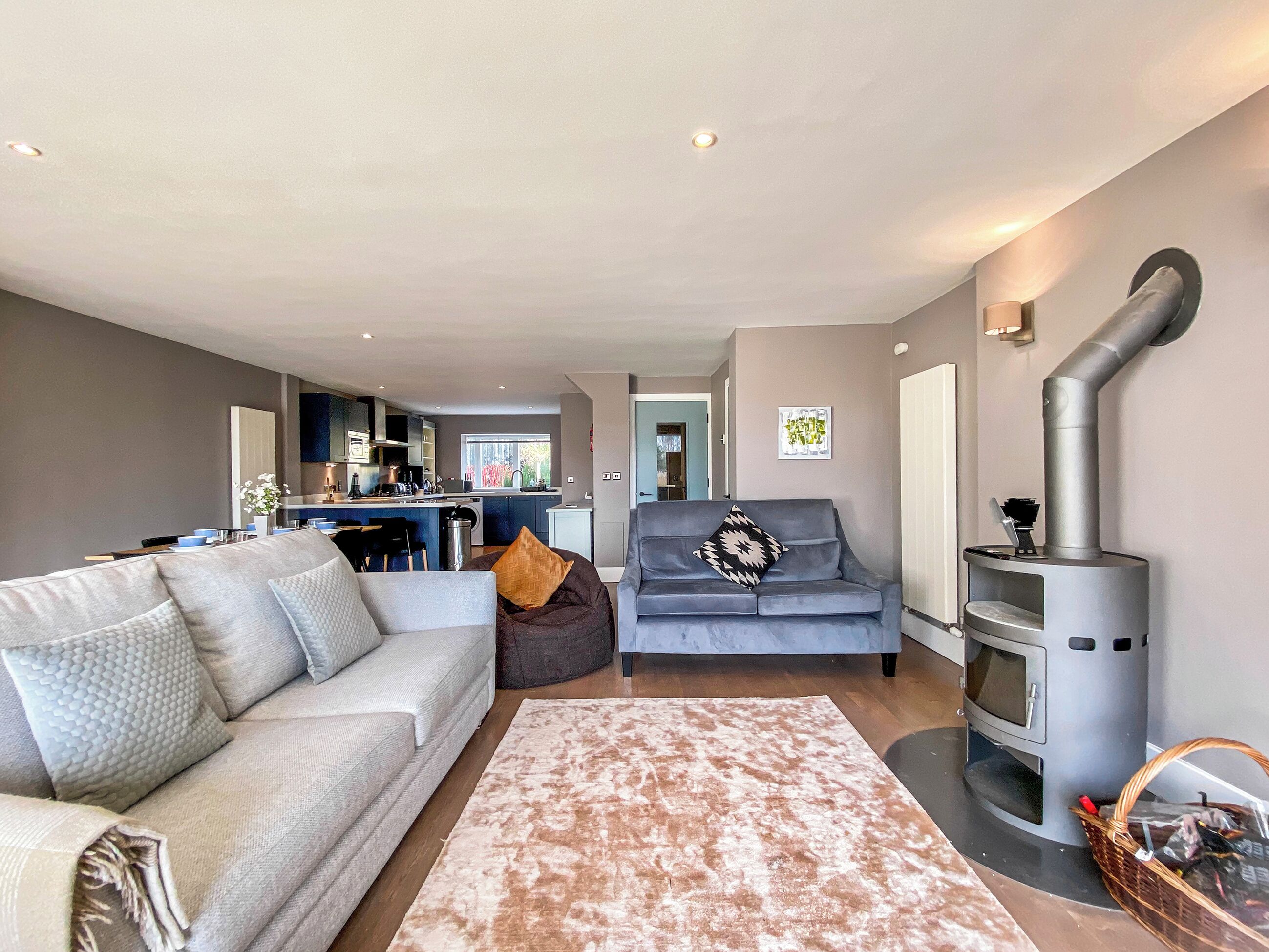 A modern living room with a grey sofa, a patterned rug, a grey armchair, and a wood-burning stove.