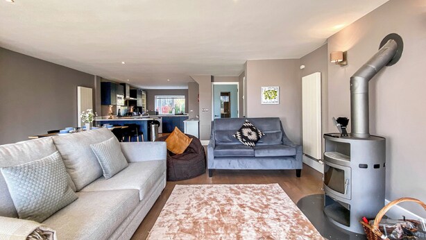 Un salon moderne avec un canapé gris, un tapis à motifs, un fauteuil gris et un poêle à bois.